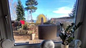 Una ventana con vista a un jardín trasero, una planta en maceta, una escultura y un objeto decorativo en el alféizar.