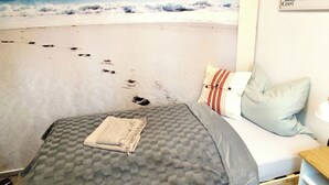 Un dormitorio con un mural de playa, una cama con ropa de cama gris y un cabecero de madera.