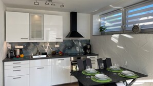 A modern kitchen with white cabinets, a black range hood, and a dining area set for two with green placemats and white plates.