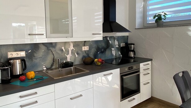 A modern kitchen with white cabinets, a black range hood, and a window with blinds.