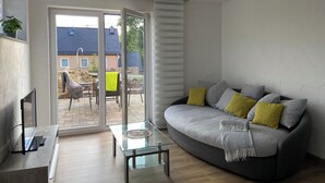 A modern living room with a grey sofa, yellow cushions, a glass coffee table, and a sliding glass door leading to an outdoor patio.