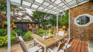 Une terrasse couverte avec une table et des chaises en bois, entourée d’une plateforme en bois et d’un mur en briques.