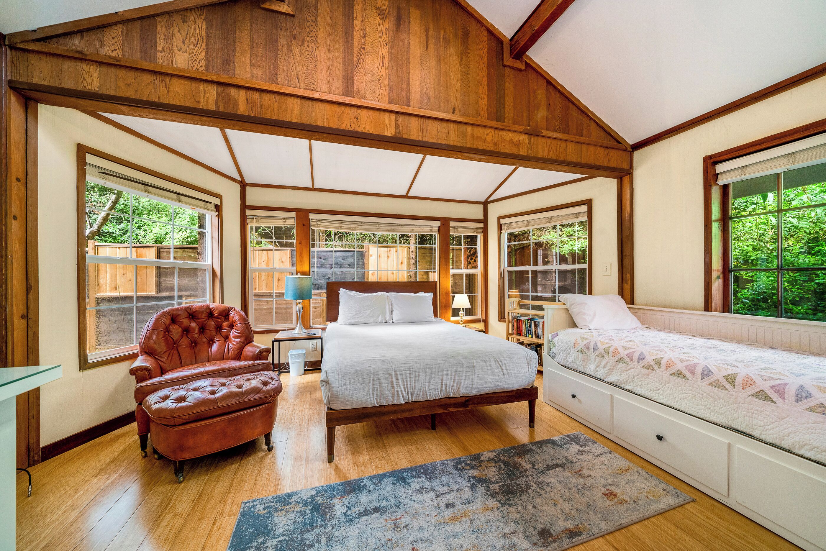 A bedroom with a large bed, a leather armchair, and a window with a view of greenery.