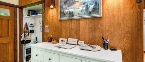 Ein Zimmer mit Holzwänden, einer weißen Kommode, einem gerahmten Landschaftsbild und einem kleinen Schreibtisch mit einer Lampe und einem Stiftekännchen.
