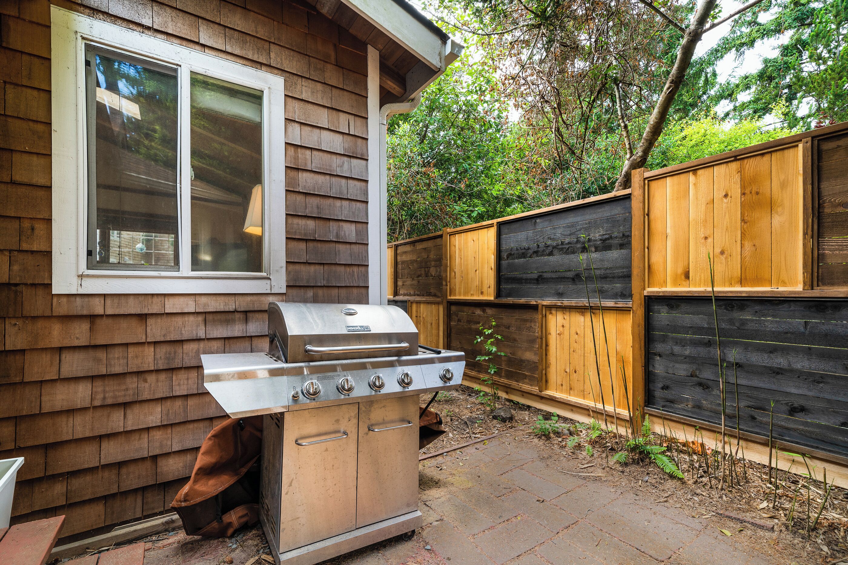 Un jardin avec un barbecue en acier inoxydable et une clôture en bois.