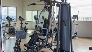Une salle de sport équipée de divers appareils d’exercice, dotée d’un grand miroir et offrant une vue sur la ville grâce à de larges fenêtres.