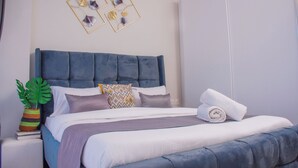 Un lit bien fait, avec une tête de lit bleue, une plante en pot et des œuvres d’art décoratives accrochées au mur.
