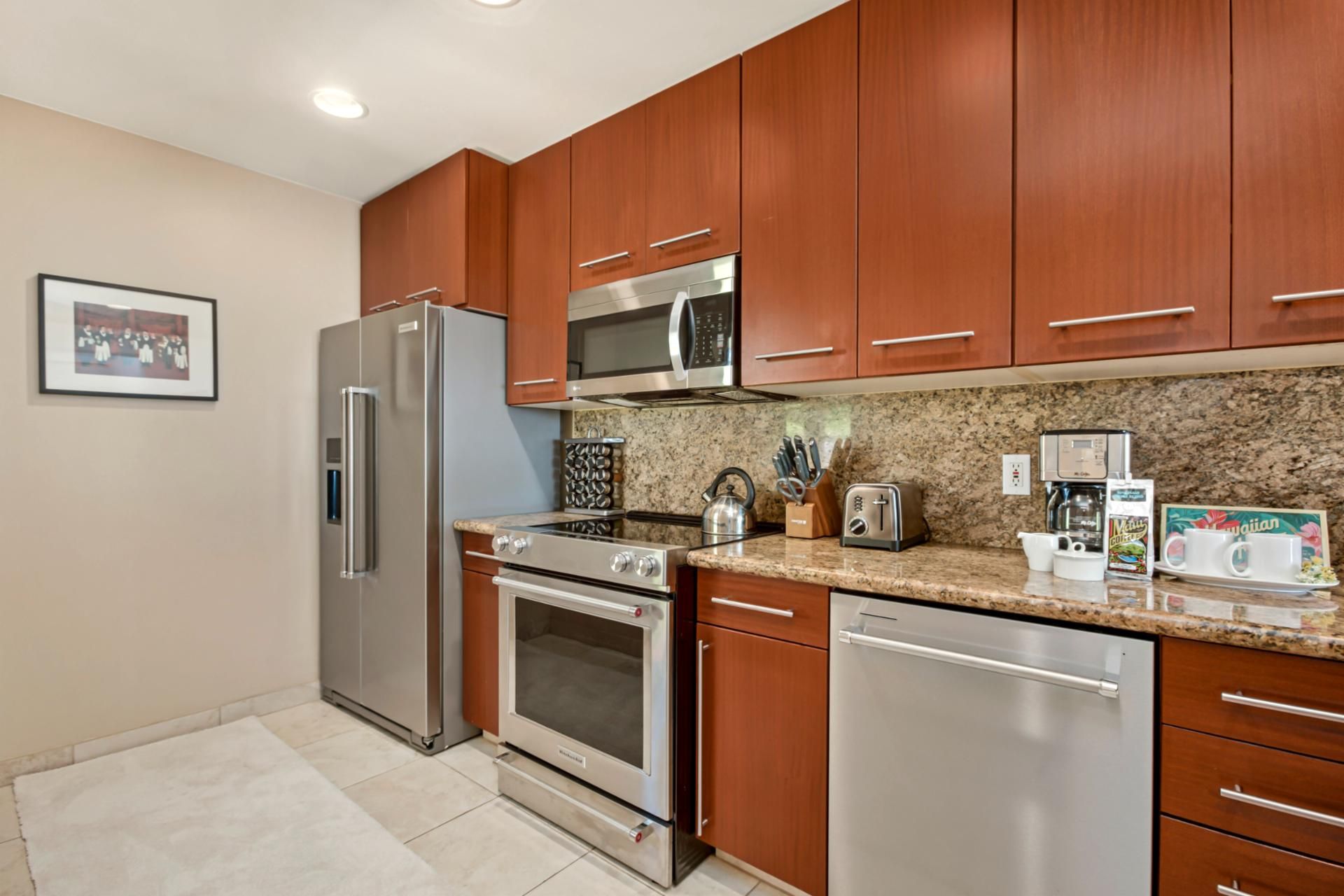 A modern kitchen with stainless steel appliances, wooden cabinets, granite countertops, and a coffee maker.