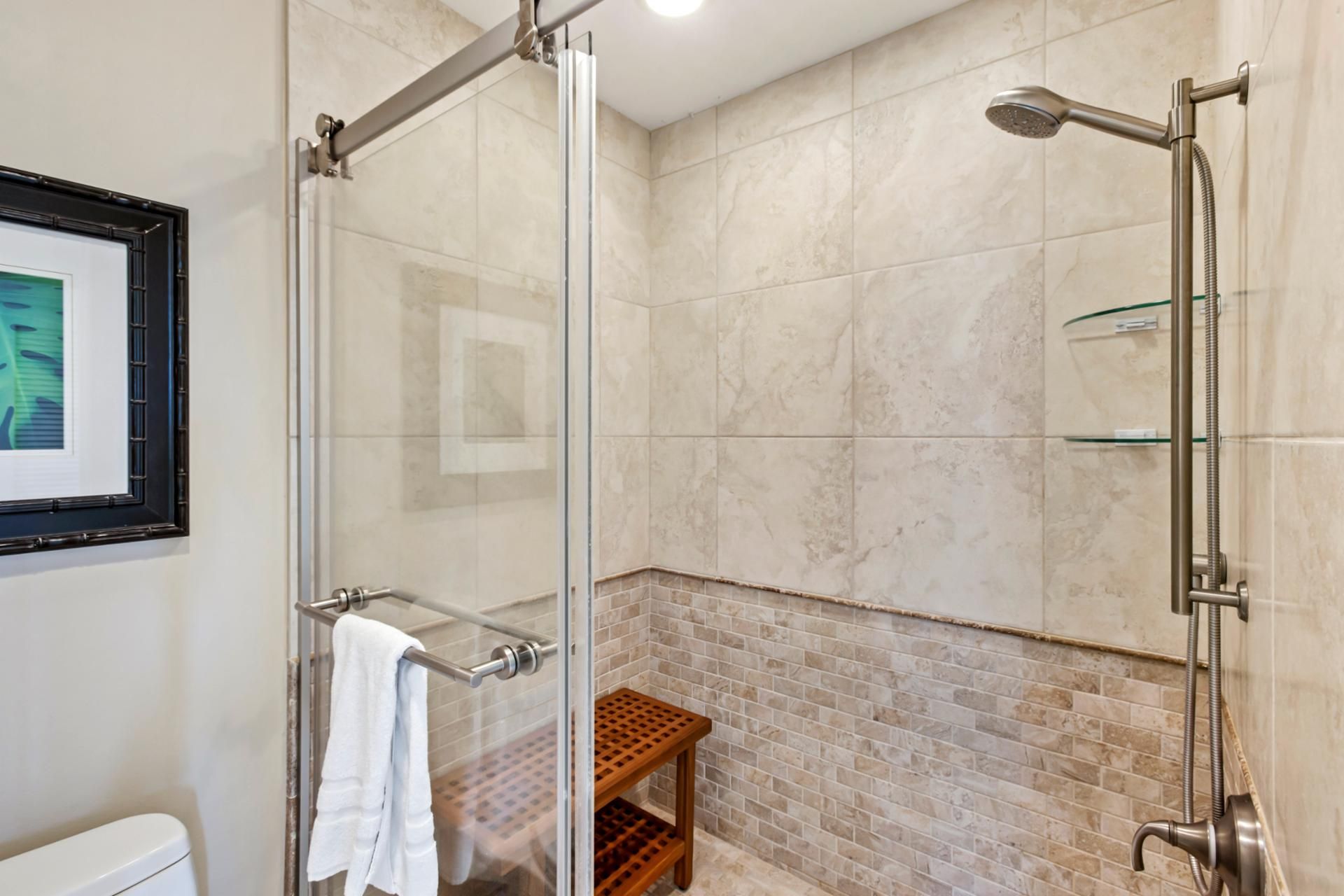 Une salle de bain moderne avec une douche à parois de verre, une étagère en verre et un banc en bois.