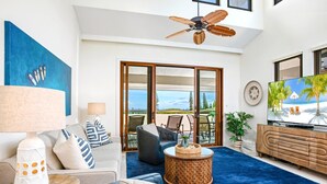A modern living room with a large TV, comfortable seating, a ceiling fan, and a view of the outdoors. - Kapalua Golf Villas | Ocean View 1 BR | Car Incl. w/ 6+ Nights | KGV-20T8 by KBM (Lahaina)