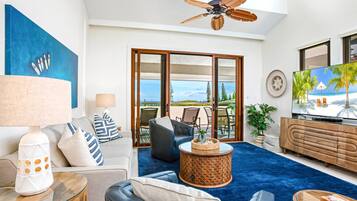 A modern living room with a large TV, comfortable seating, a ceiling fan, and a view of the outdoors.