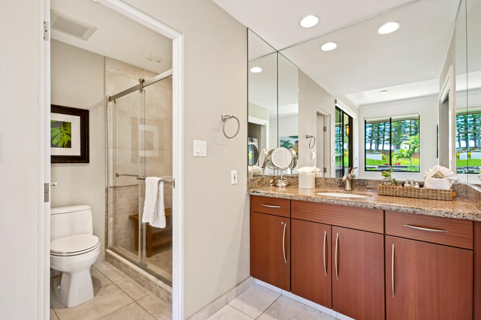 A modern bathroom with a glass shower, a white toilet, wooden cabinets, and a large mirror.