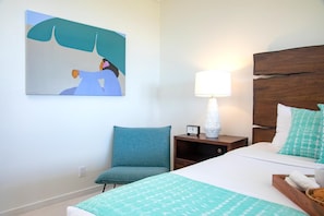 Um quarto com cama, poltrona, mesa de cabeceira com abajur e um quadro na parede.