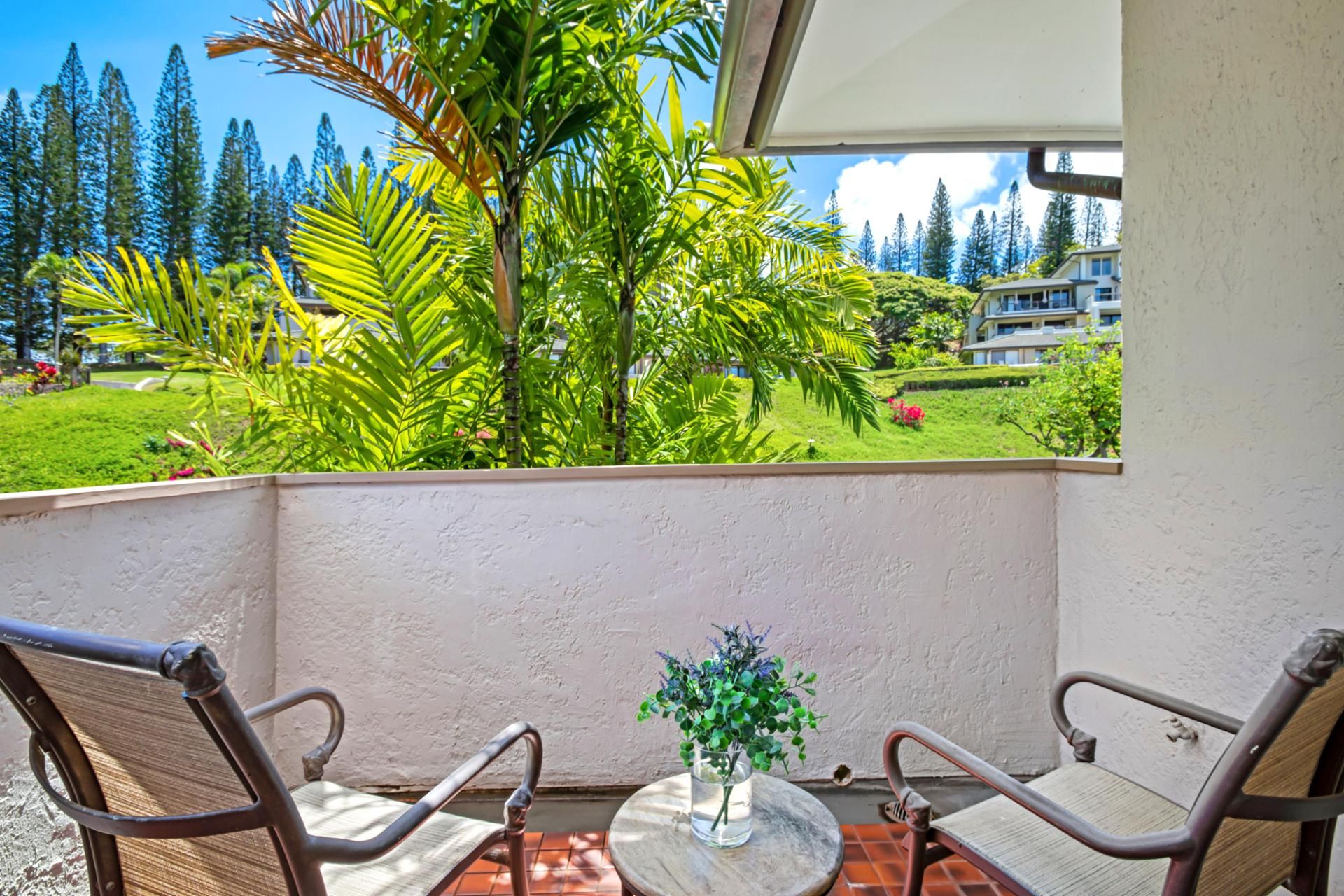 A balcony with two chairs and a small table, overlooking a lush garden and a residential area.