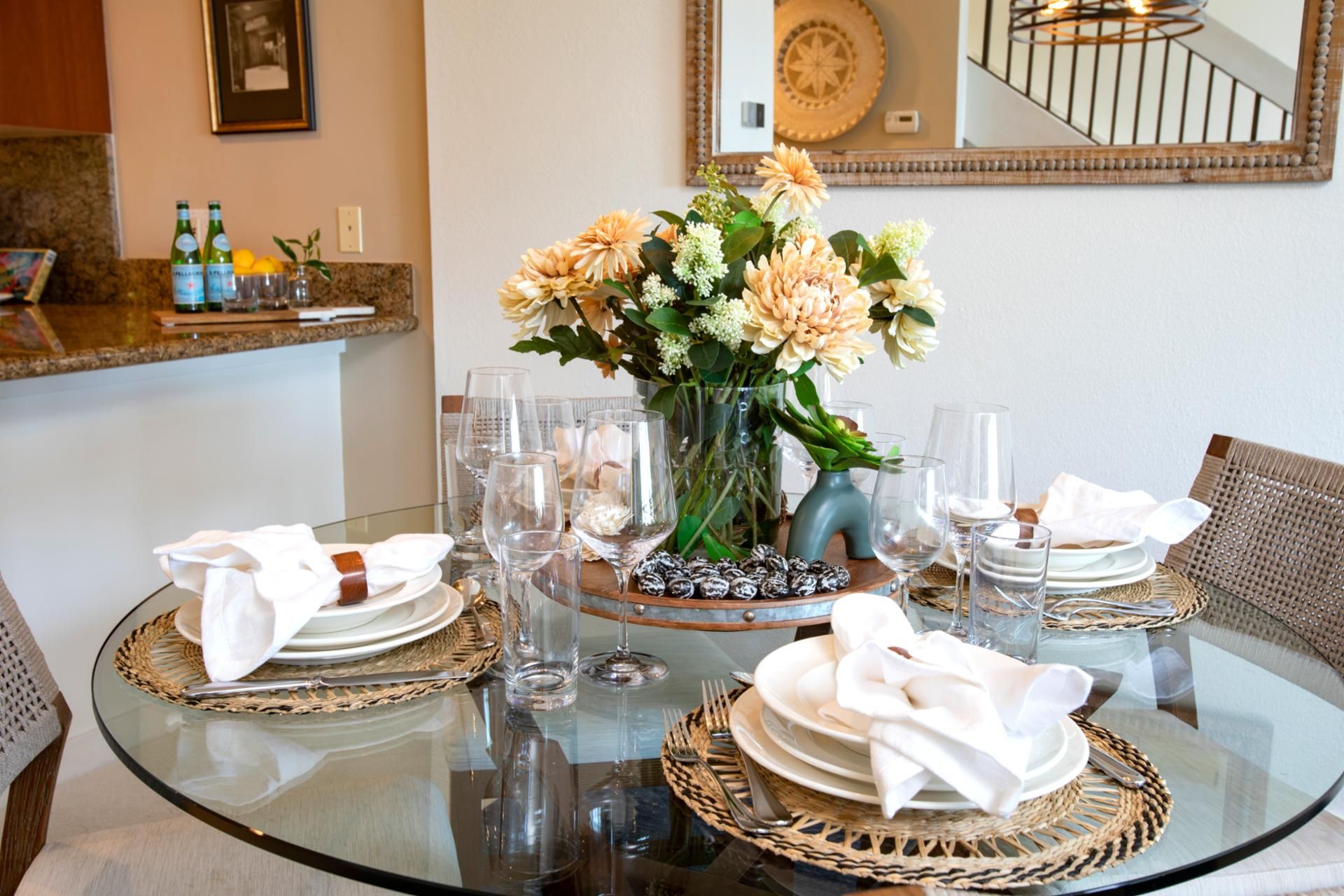 A dining table set for four with clear glassware, a vase of flowers, and woven placemats.