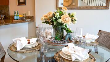 A dining table set for four with clear glassware, a vase of flowers, and woven placemats.