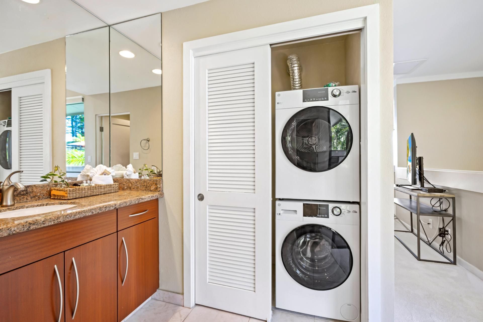 A laundry room with two stacked front-loading washing machines and a dryer, a countertop with a sink and toiletries, and a mirror reflecting the room.
