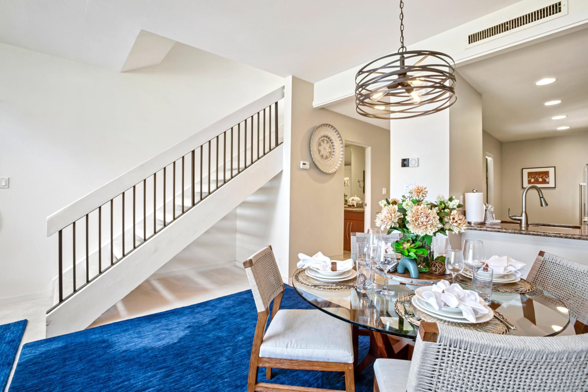 A dining area with a glass table, white chairs, and a blue rug.
