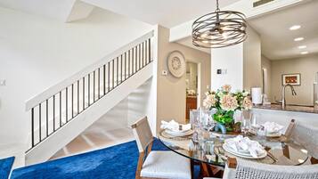 A dining area with a glass table, white chairs, and a blue rug.