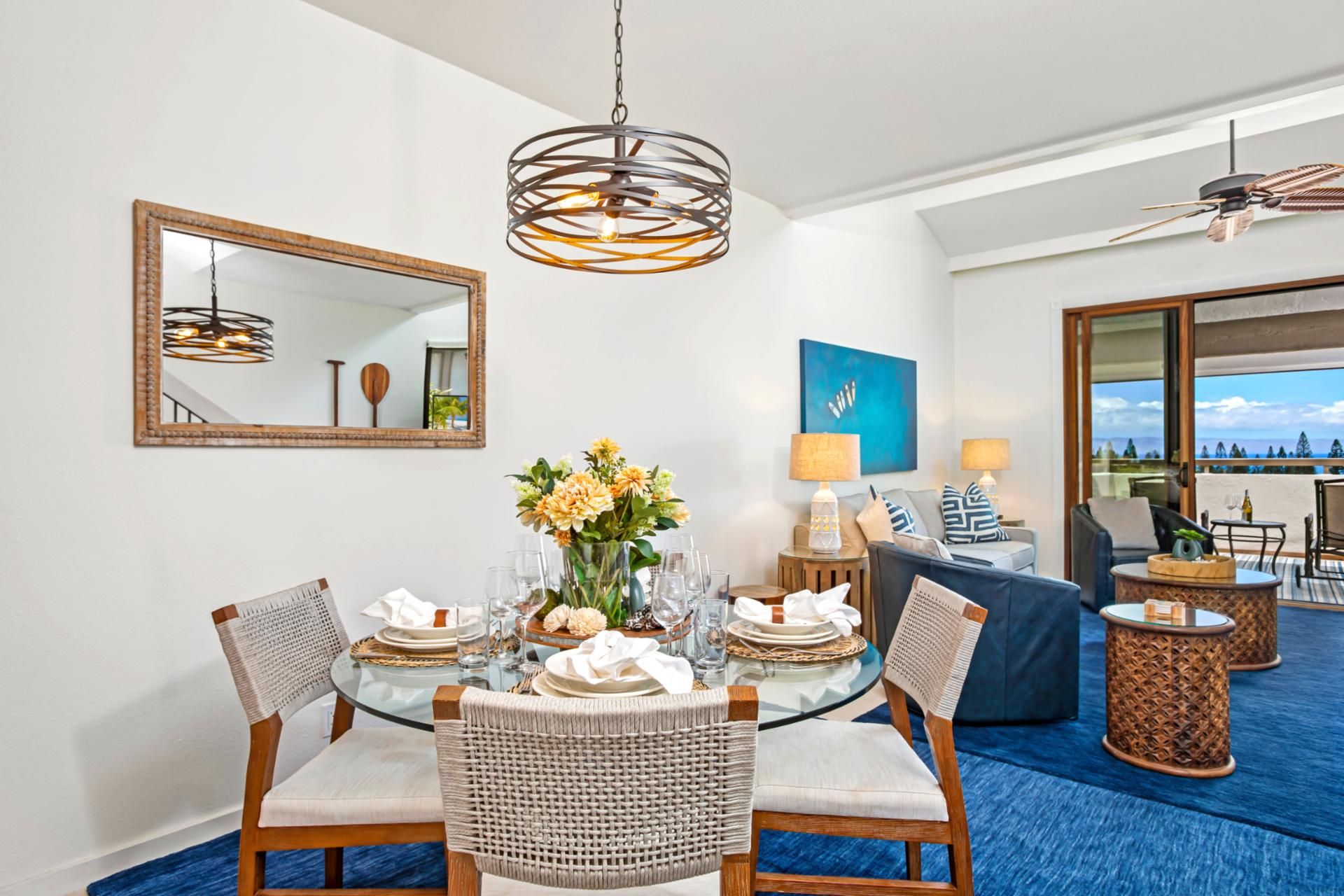 A dining area with a round glass table, wicker chairs, and a hanging light fixture.