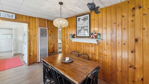 Une pièce aux murs lambrés, comprenant une table à manger, des chaises, une pancarte « BIENVENUE », un tableau encadré et une étagère ornée d’objets décoratifs.