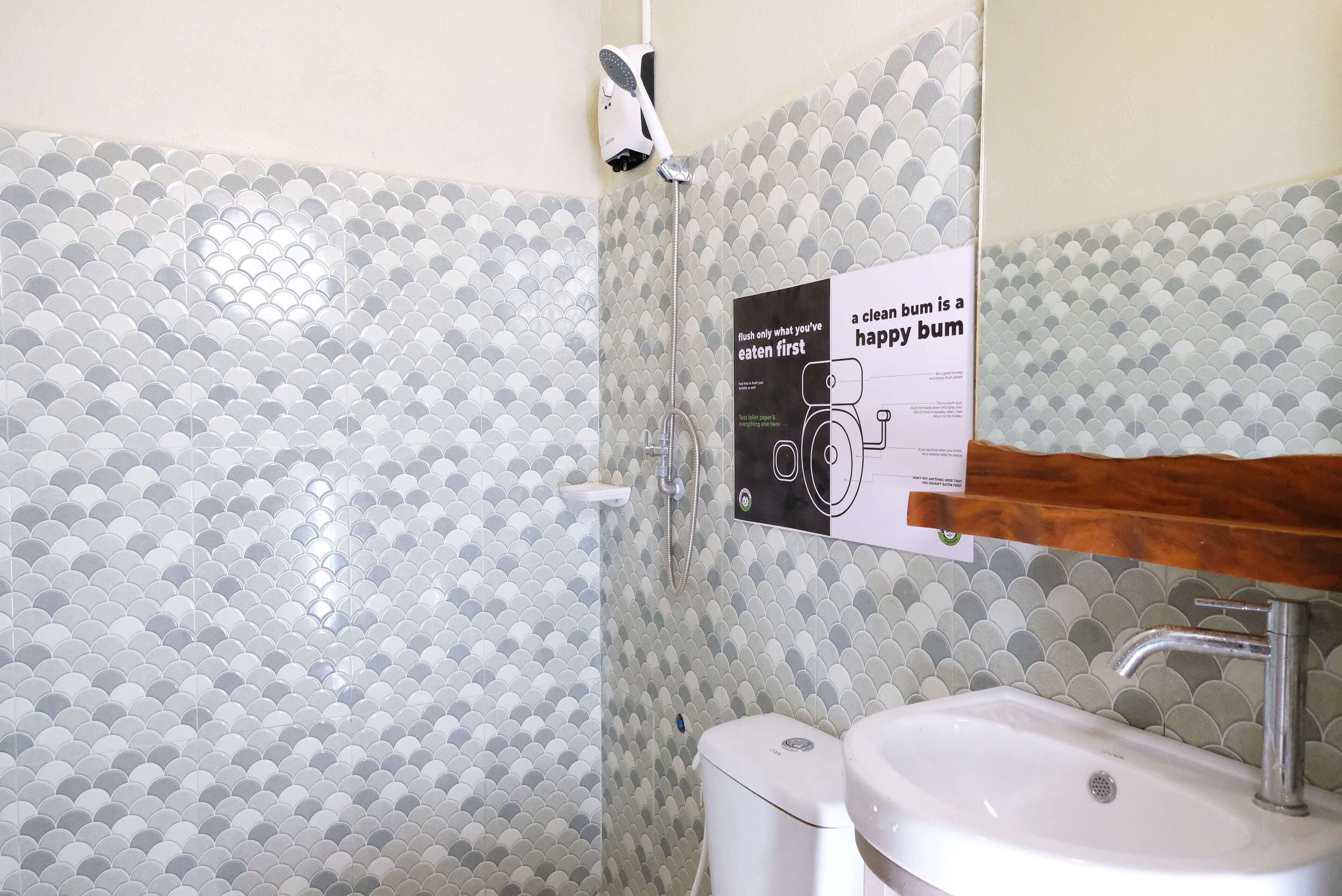 A bathroom with a tiled wall featuring a scalloped pattern, a white toilet, a sink with a wooden countertop, and a poster on the wall.