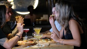 Een houten tafel met pizza's en een martini.