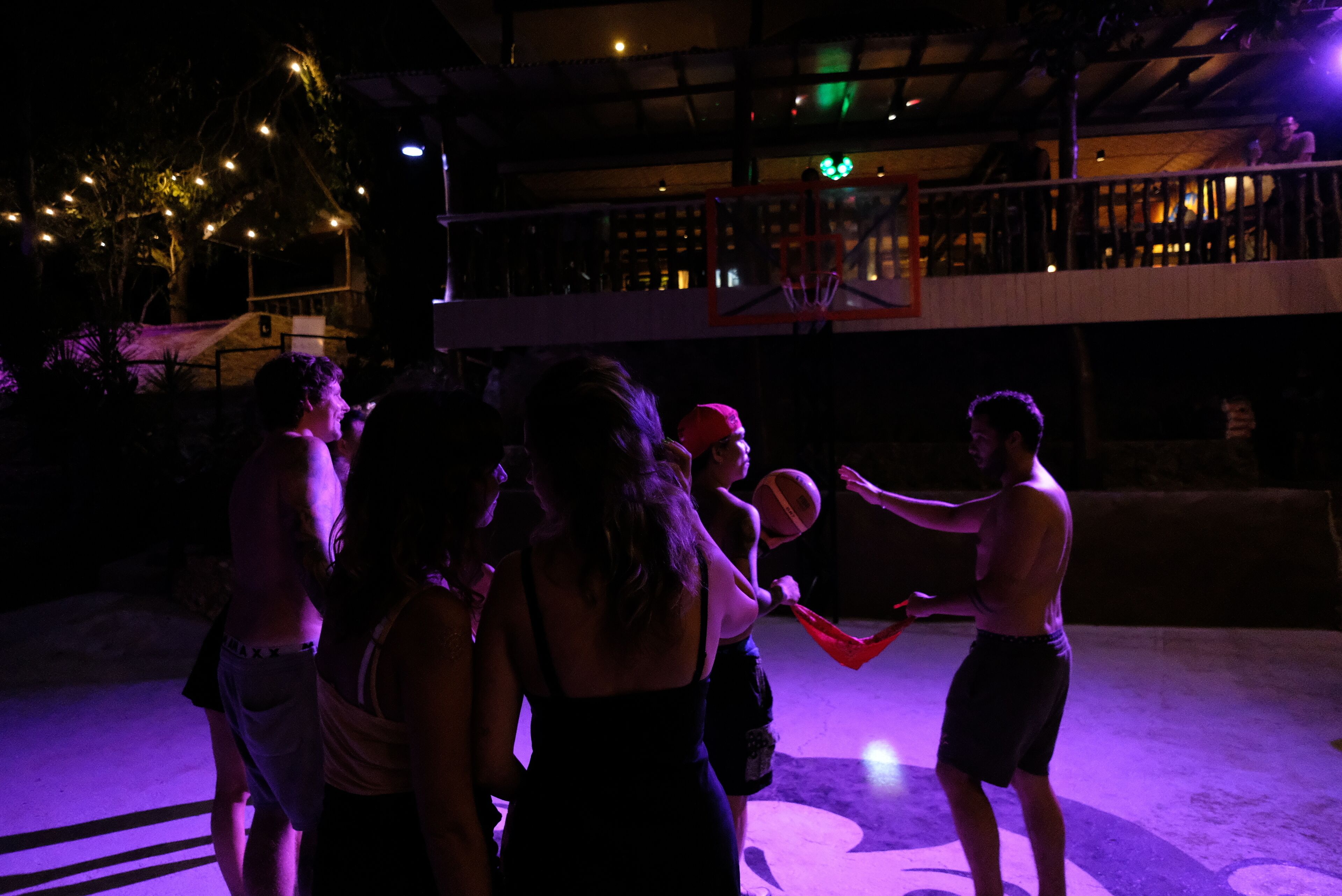 Eine Gruppe von Menschen spielt nachts Basketball auf einem Außenplatz.