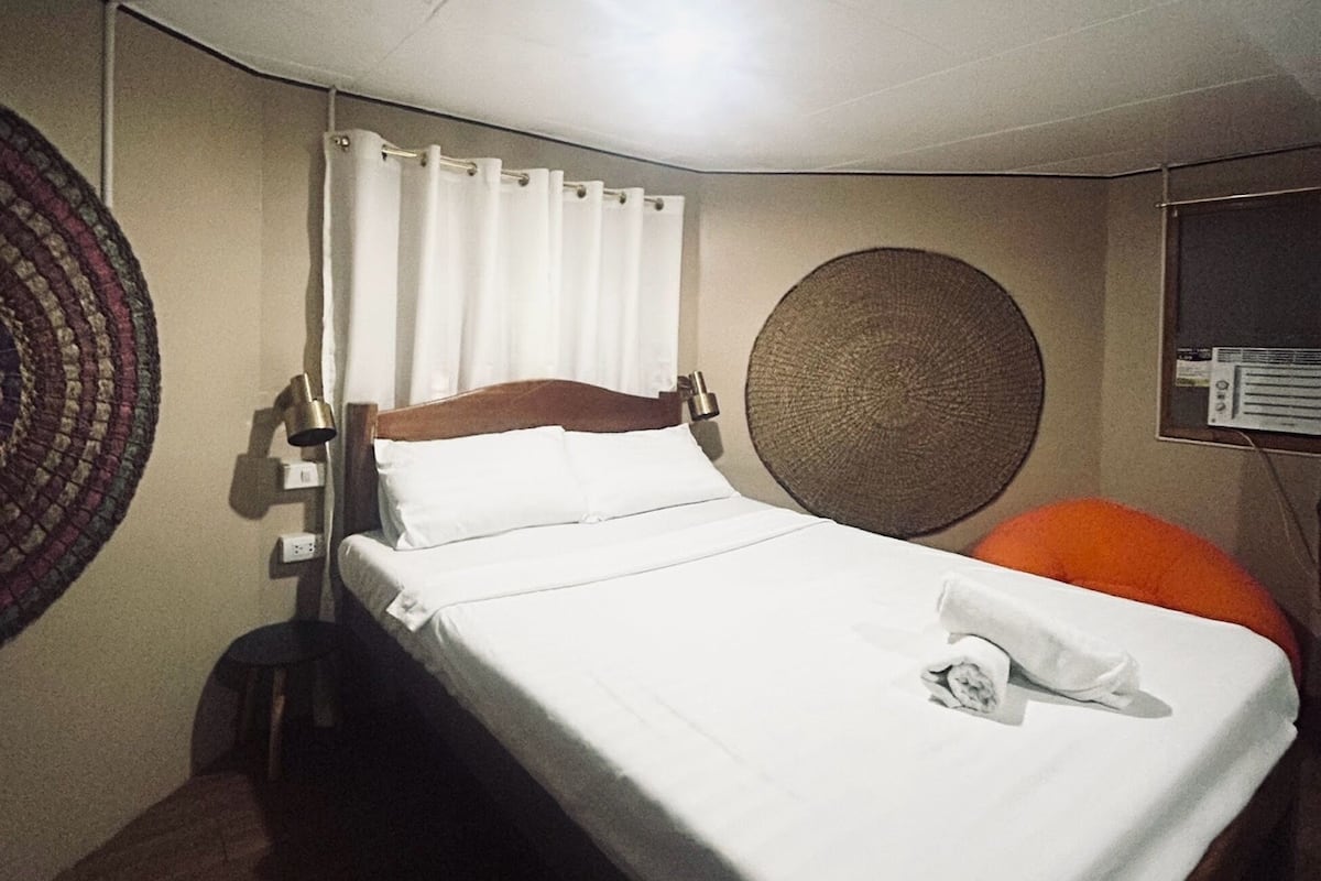 Quarto de hotel com cama, uma cadeira, decoração circular na parede e ar condicionado fixado na parede.