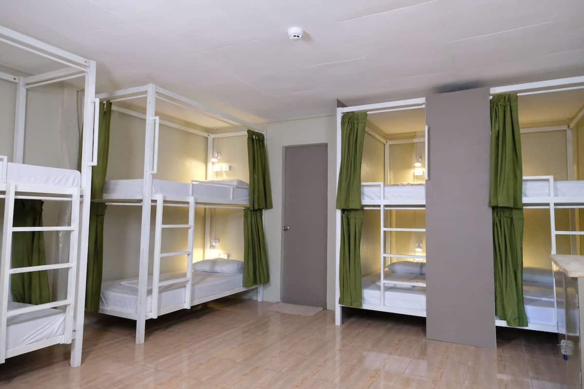 Quarto com beliches, cortinas verdes e uma porta.