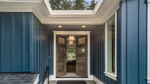 Un escalier menant à une porte dotée d’un panneau de verre, une lucarne au-dessus, et une vue sur la verdure à l’extérieur.