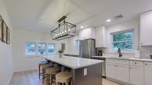 A modern kitchen with a central island, bar stools, white cabinetry, stainless steel appliances, and a large window providing natural light. - New! Sleeps 16! Across from Sight&Sound! Location! (Ronks)