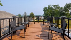 A wooden deck with outdoor seating, a railing, and a view of trees and buildings in the distance. - New! Sleeps 16! Across from Sight&Sound! Location! (Ronks)