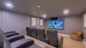 A home theater room with a large flat-screen TV, multiple black leather recliners, a wooden coffee table, and a tan bean bag. - New! Sleeps 16! Across from Sight&Sound! Location! (Ronks)
