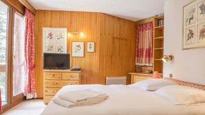 A bedroom with a large bed, wooden panel walls, a television, and a bookshelf. - Charming Ski Apartment in Courchevel 1850 (Courchevel)