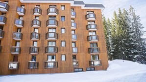 A multi-story wooden building with balconies, surrounded by snow and trees. - Charming Ski Apartment in Courchevel 1850 (Courchevel)