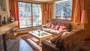 A cozy living room with a fireplace, a sofa, a coffee table, and large windows with curtains. - Charming Ski Apartment in Courchevel 1850 (Courchevel)