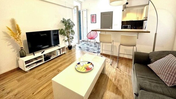 En moderne stue med et fladskærms-tv, et sofabord, en sofa og et spiseområde med stole.