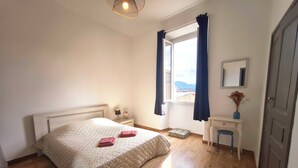 Et soveværelse med seng, natbord, lampe, vindue med gardiner og udsigt ud.