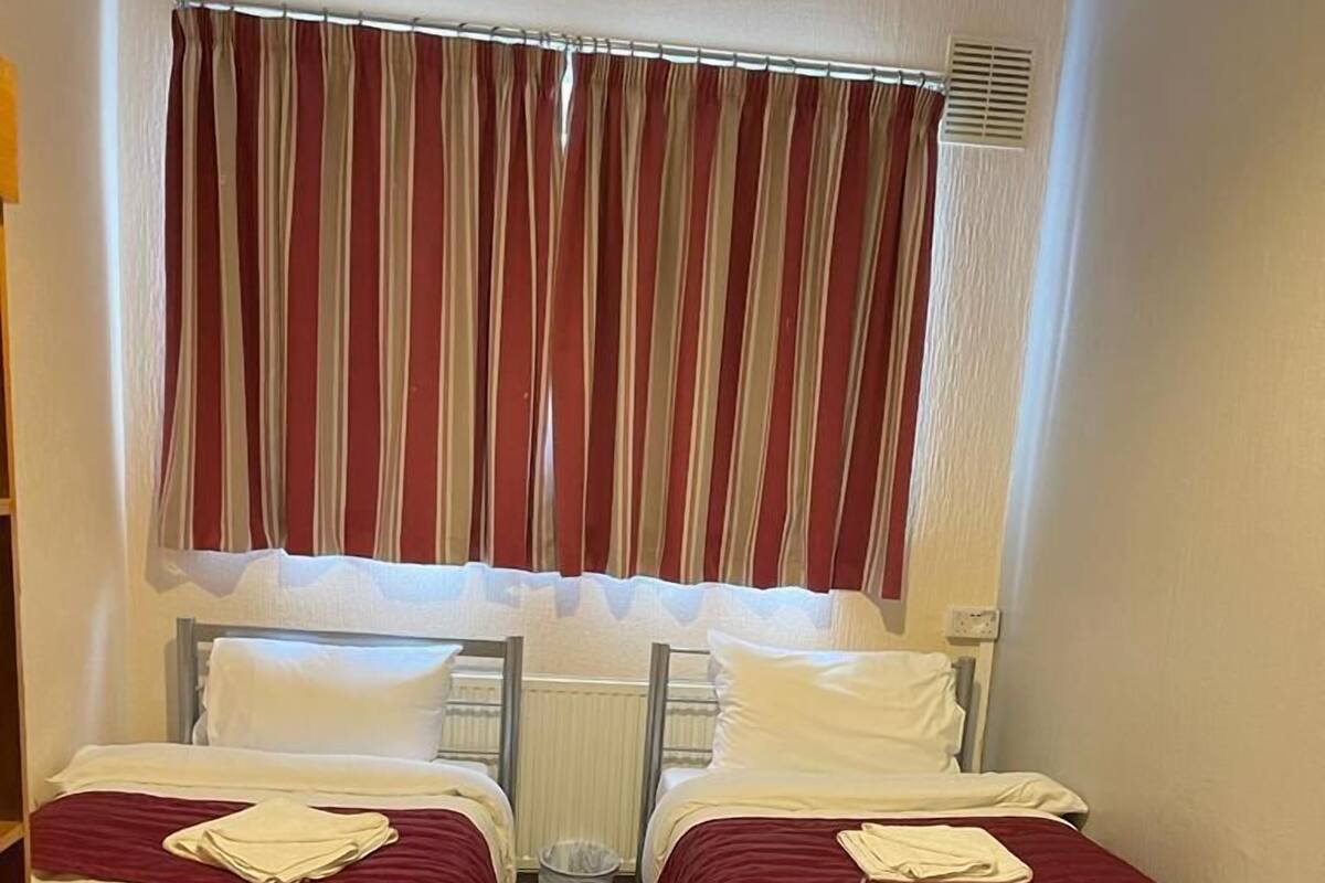 A room with two single beds, a small table, and a window with striped curtains.