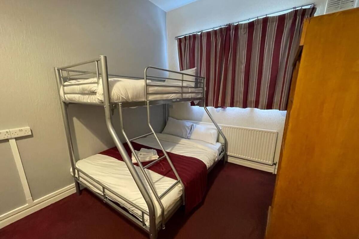 A bunk bed room with a window, curtains, and a radiator.