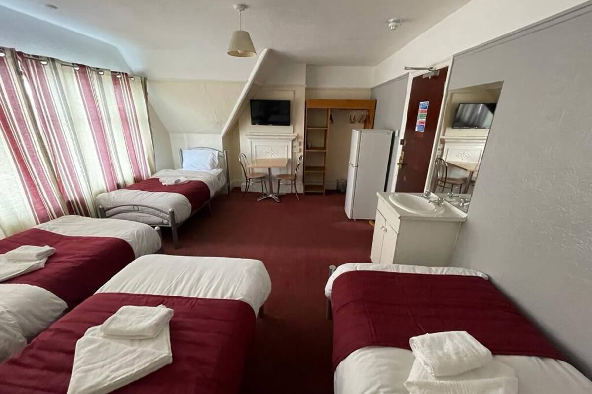 A hotel room with four beds, a desk, a television, a refrigerator, and a bathroom.