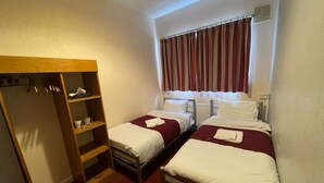 A hotel room with two single beds, a wooden wardrobe, and a window with curtains. - St Nicholas Hotel Kenton (Harrow)