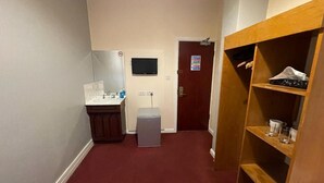 A hallway with a sink, a small refrigerator, and a wooden shelving unit with items on it. - St Nicholas Hotel Kenton (Harrow)