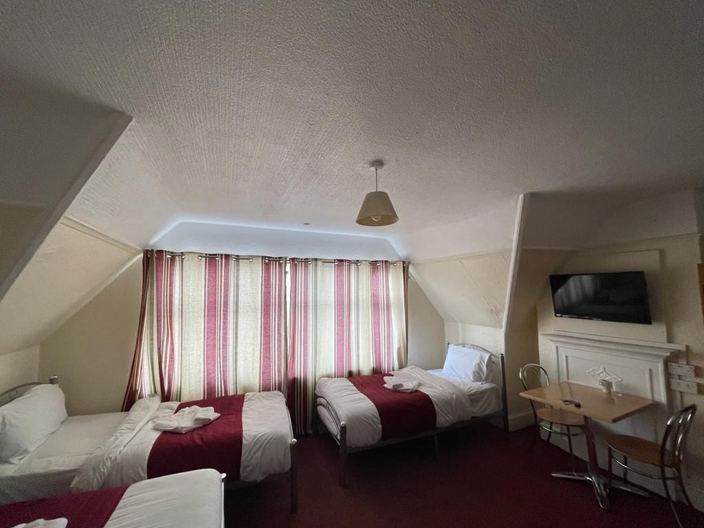 A hotel room with two beds, a dining table, a TV, and a fireplace.