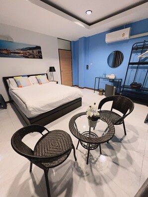 A modern bedroom with a large bed, two wicker chairs, a small table with flowers, and a view of the city through a window. - Noc House (Bangkok)