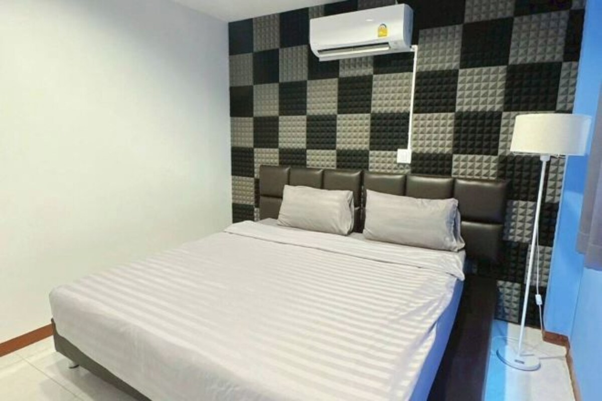 A hotel room with a bed, a wall-mounted air conditioner, and a patterned wall.