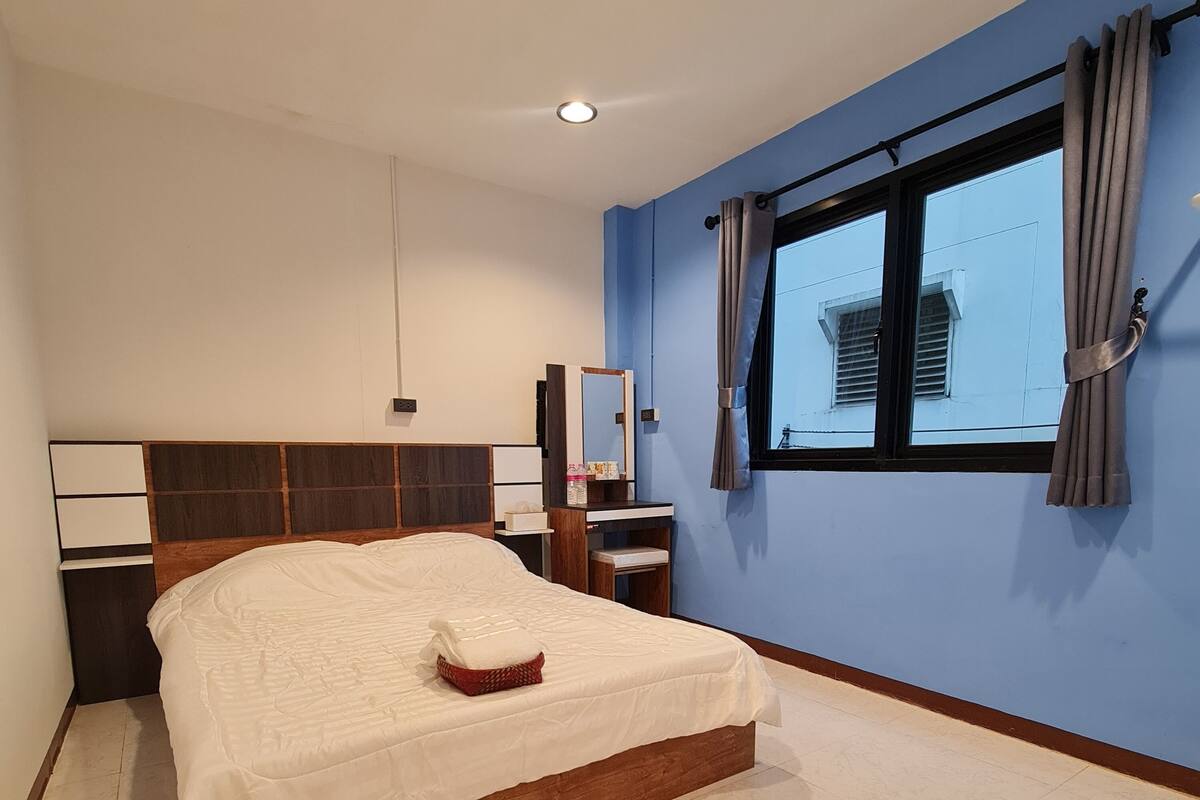 A modern hotel room with a large bed, a bedside table, a mirror, and a window with curtains.