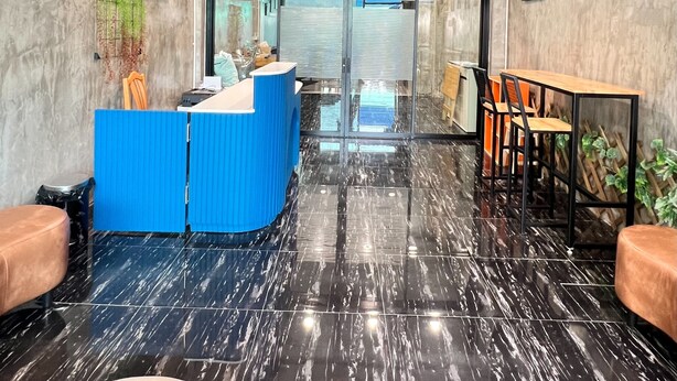 A modern reception area with a blue counter, black marble flooring, and a large window offering a view of the outside. - Noc House (Bangkok)