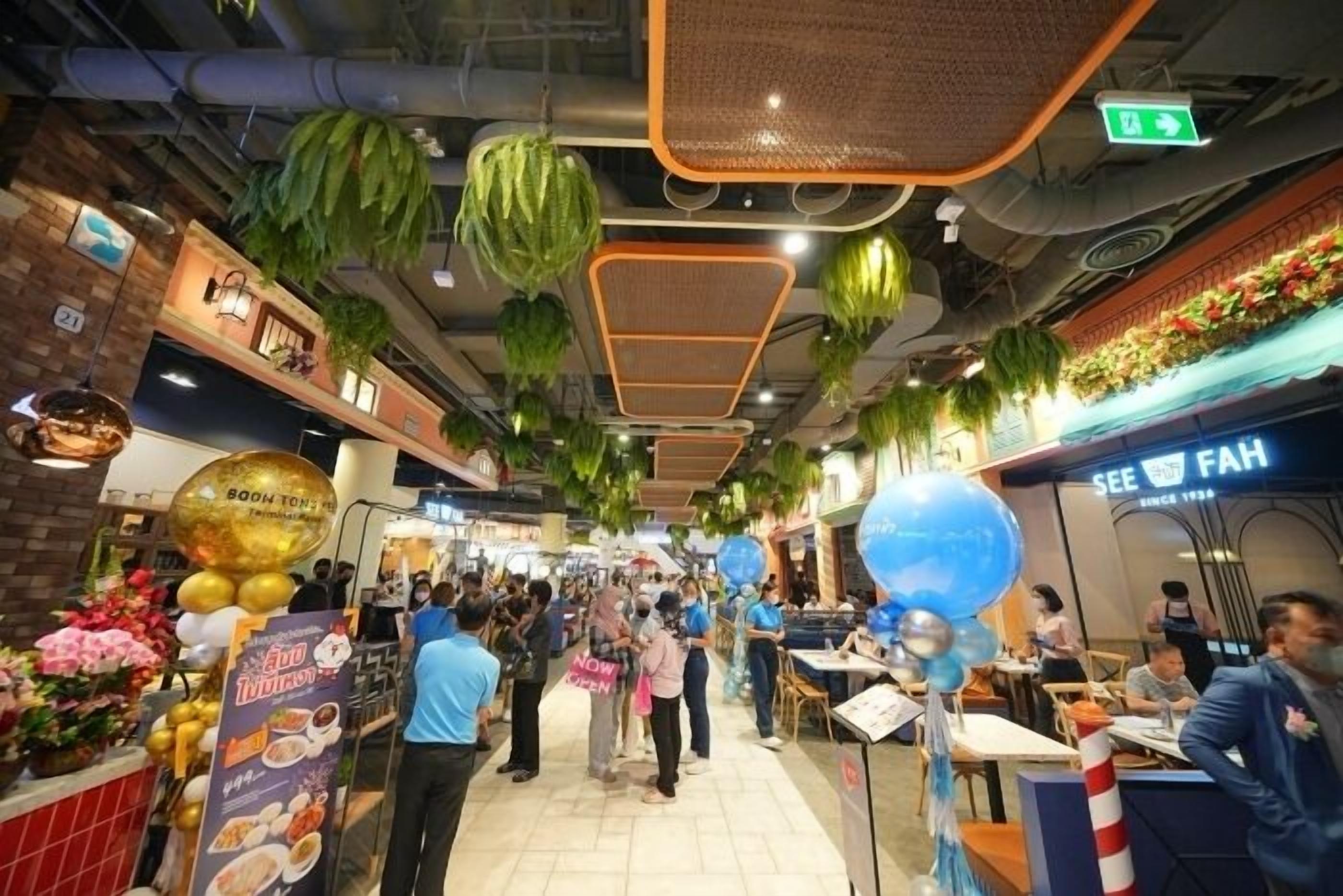 A bustling indoor market with hanging plants, food stalls, and people shopping.